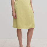 A person wearing a pale yellow knee-length Emmy Wrap Skirt by Herskind ApS, featuring an A-line silhouette tied at the waist with a simple side bow and black flat shoes.