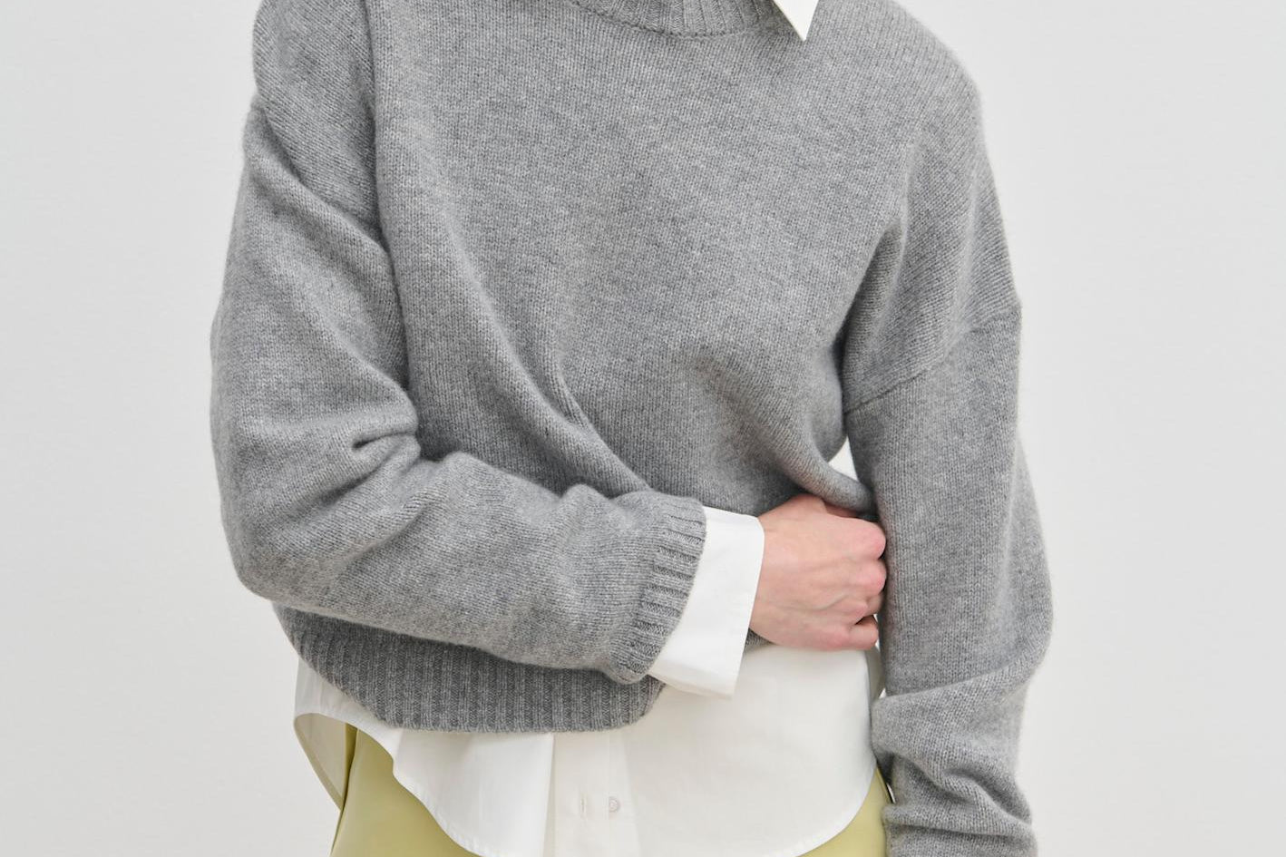 A model wears a grey Constantine Cashmere Knit Blouse by Herskind ApS over a white collared shirt and a pale yellow skirt.