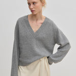 A person wearing a grey V-neck Micky Cashmere Knit Blouse by Herskind ApS and a cream wrap skirt.