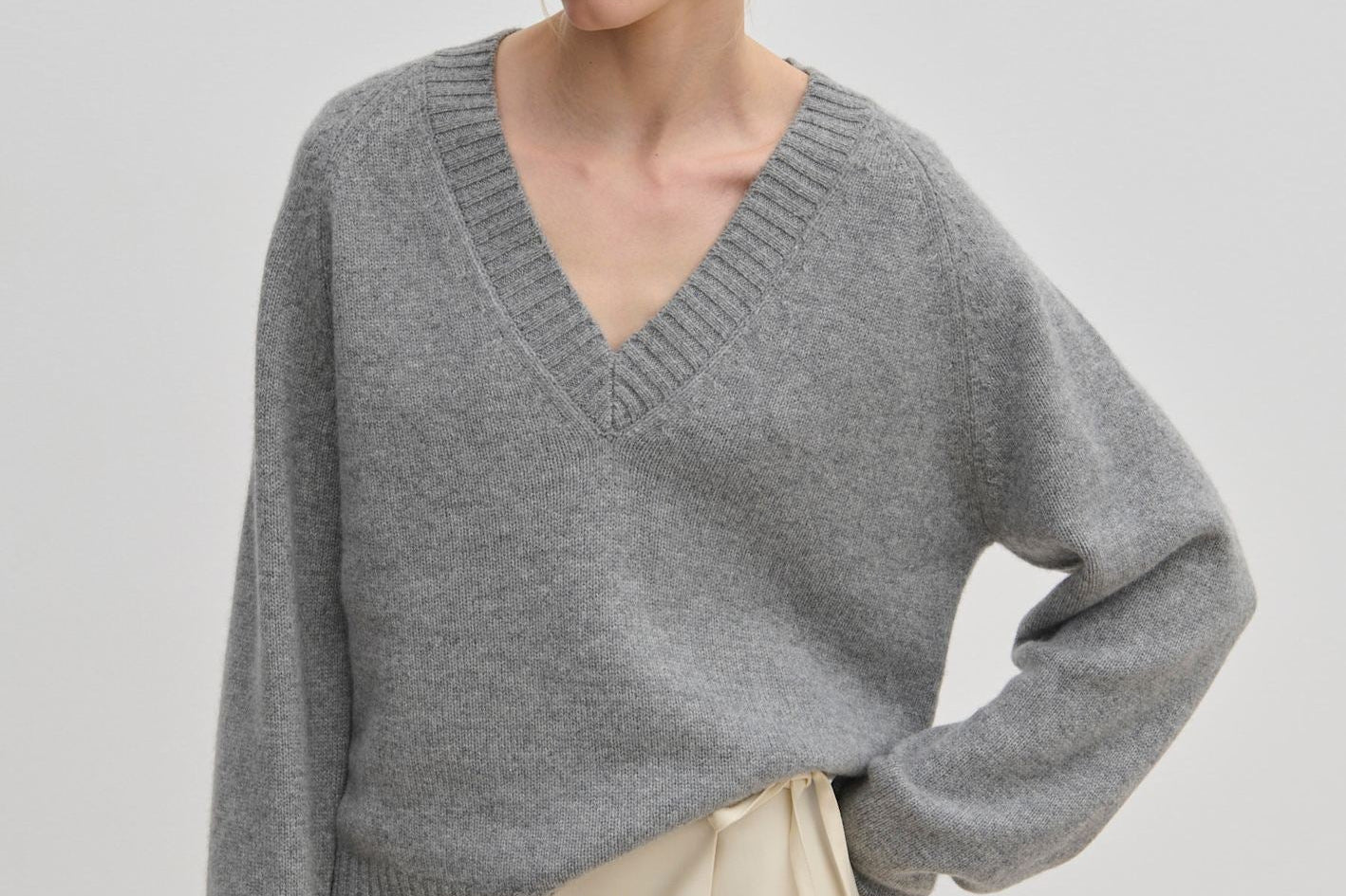 A person wearing a grey V-neck Micky Cashmere Knit Blouse by Herskind ApS and a cream wrap skirt.