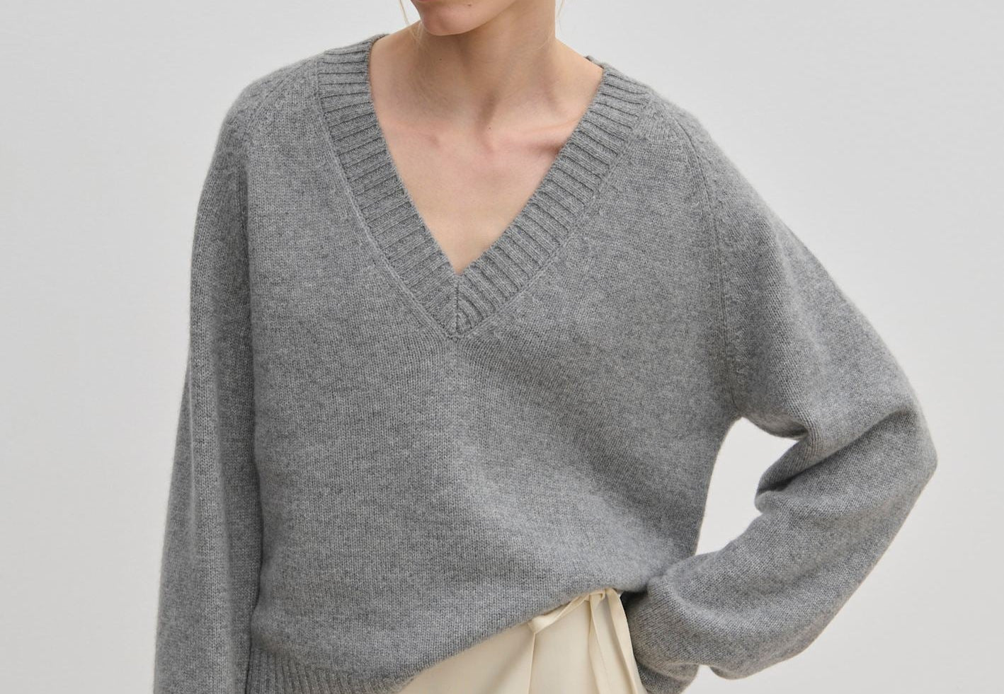 A person wearing a grey V-neck Micky Cashmere Knit Blouse by Herskind ApS and a cream wrap skirt.
