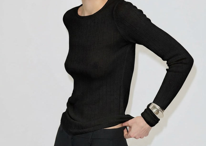 A person wears a black Camb Knit Blouse by Herskind ApS in fine-knit merino wool tucked into black trousers.