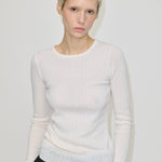 A person wearing the Herskind ApS Camb Knit Blouse, a long-sleeved, white merino wool ribbed knit top with pointelle detailing.
