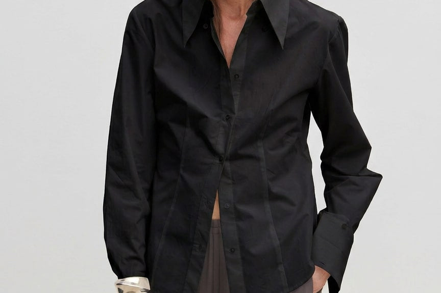 A slim-fit, long-sleeved black Vivienne Shirt by Herskind ApS with a pointed collar and wide cuffs, worn over grey trousers.