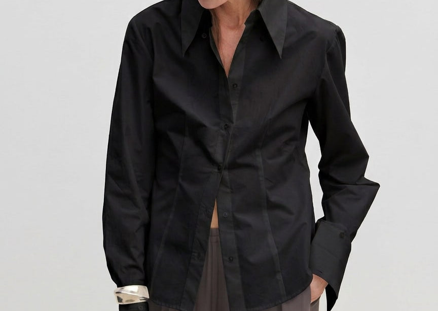 A slim-fit, long-sleeved black Vivienne Shirt by Herskind ApS with a pointed collar and wide cuffs, worn over grey trousers.
