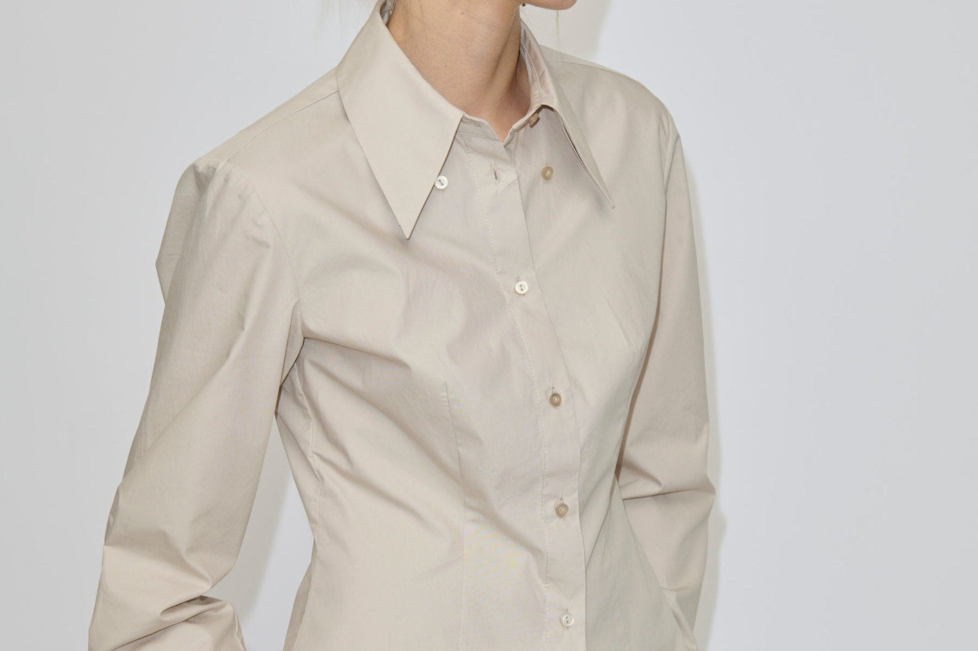 A slim fit, beige Vivienne Shirt by Herskind ApS featuring long sleeves and a pointed collar, paired with dark grey trousers.