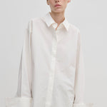 A model wears the Herskind ApS Inga Shirt, a crisp, oversized white button-down with a point collar and wide, folded cuffs.