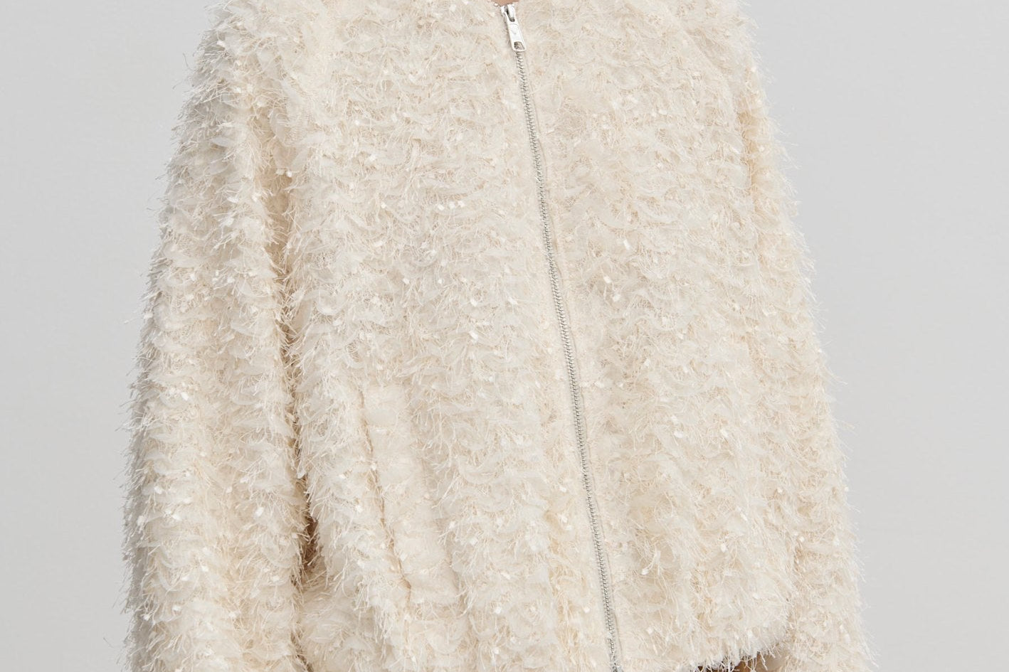 A person wears a cream-colored, relaxed-fit Jimi Bomber Jacket by Herskind ApS, featuring a textured, fringed finish and balloon sleeves.