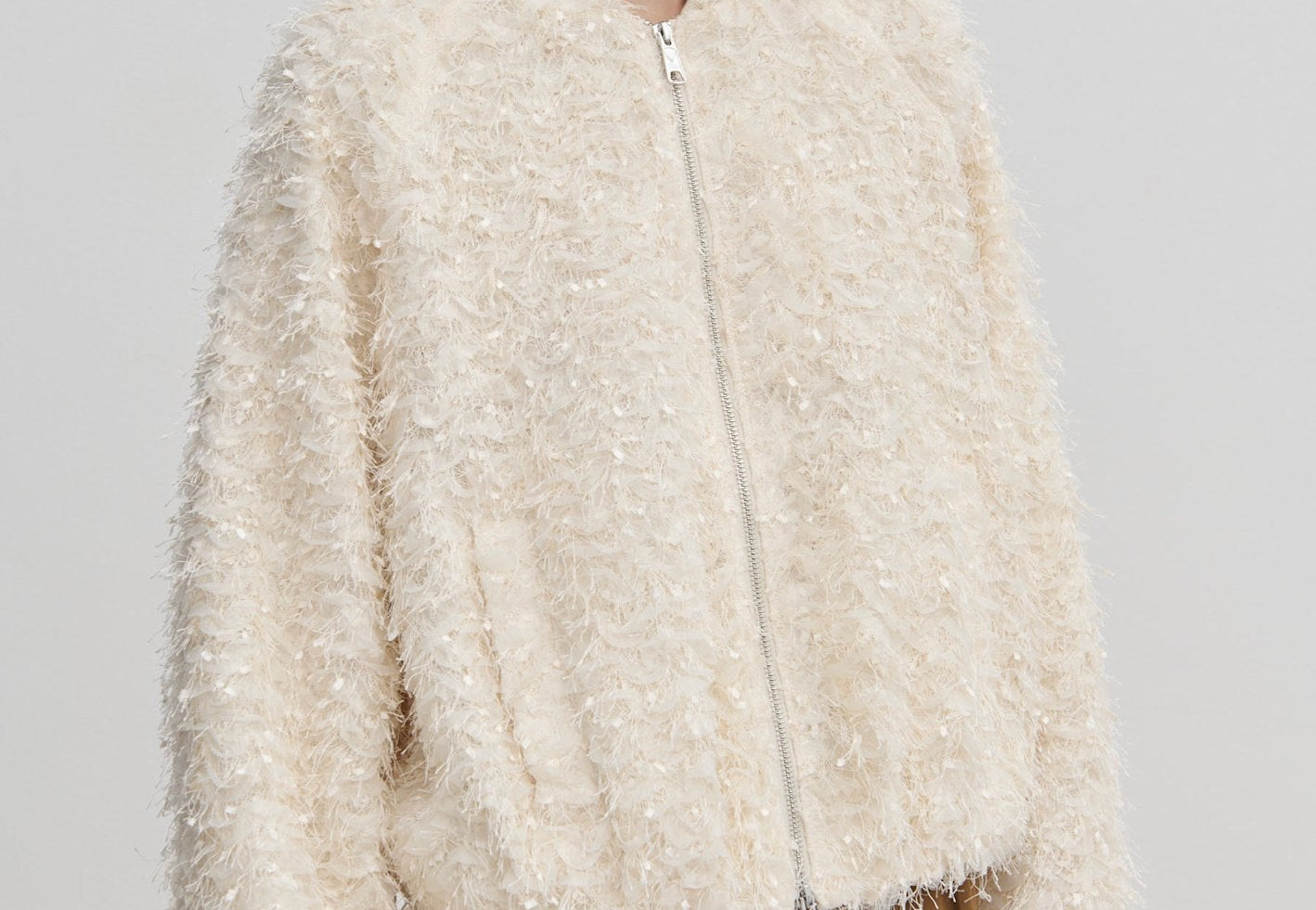 A person wears a cream-colored, relaxed-fit Jimi Bomber Jacket by Herskind ApS, featuring a textured, fringed finish and balloon sleeves.