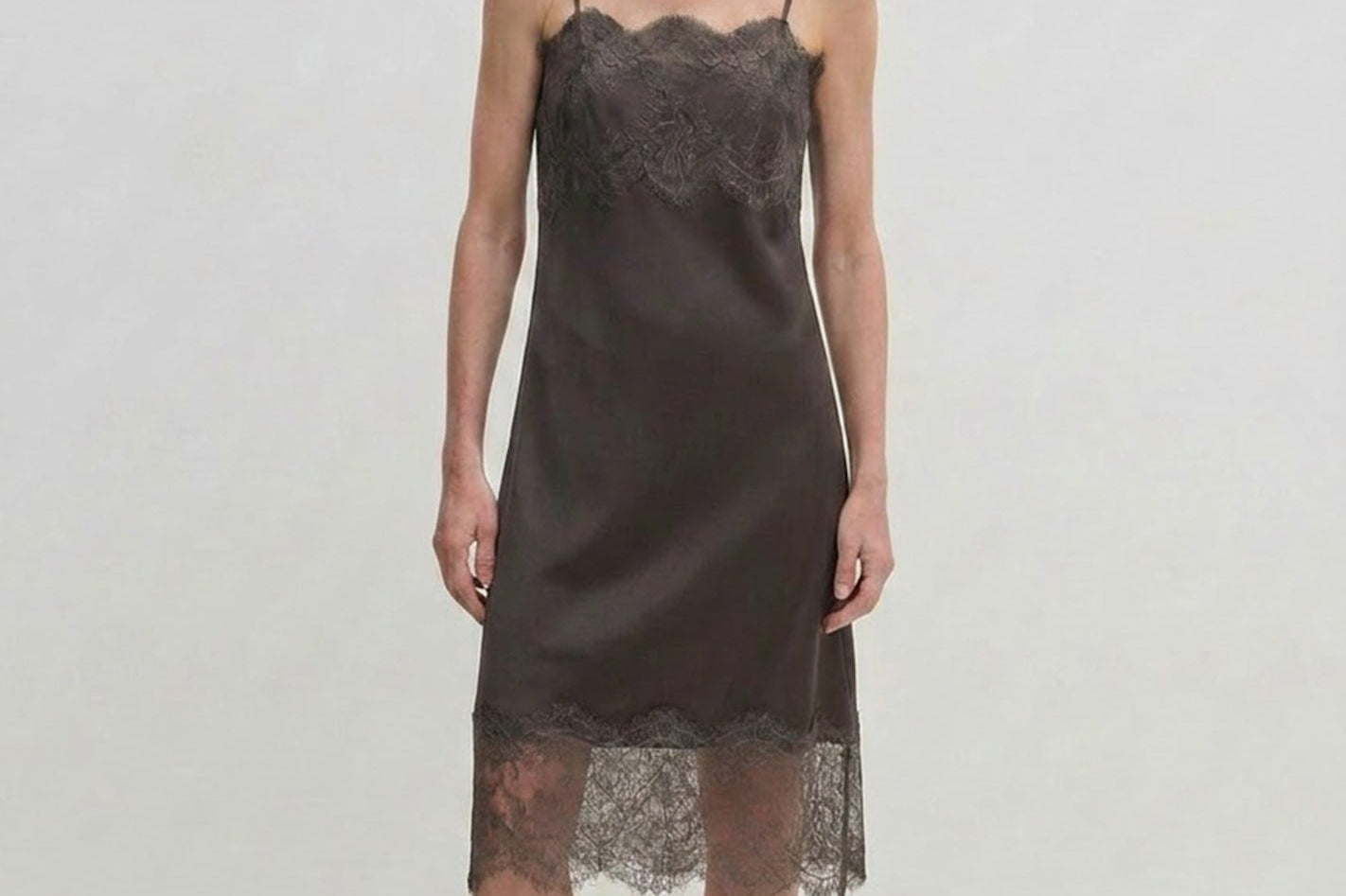 A person wears a dark midi-length Linus Dress by Herskind ApS with a lace-trimmed hem, paired with light-colored pointed-toe heels.