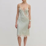 Herskind ApS Luna Dress in sage green FSC viscose, featuring delicate lace trim along the neckline, hem, and side slit of this midi slip dress.