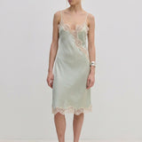 Herskind ApS Luna Dress in sage green FSC viscose, featuring delicate lace trim along the neckline, hem, and side slit of this midi slip dress.