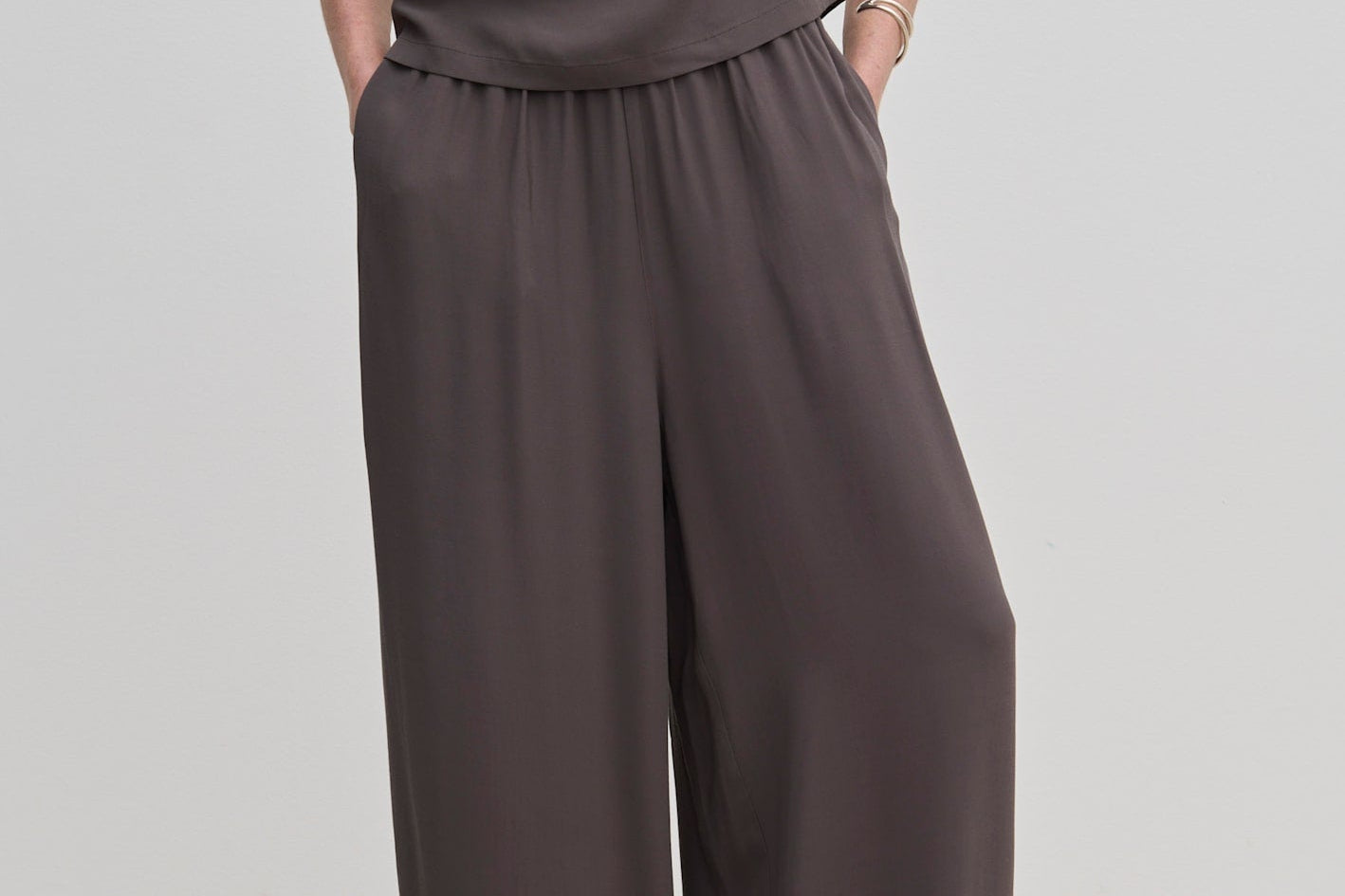 A person wears dark gray Nya Pants by Herskind ApS, featuring balloon legs, an elasticated waist, and a draped top.