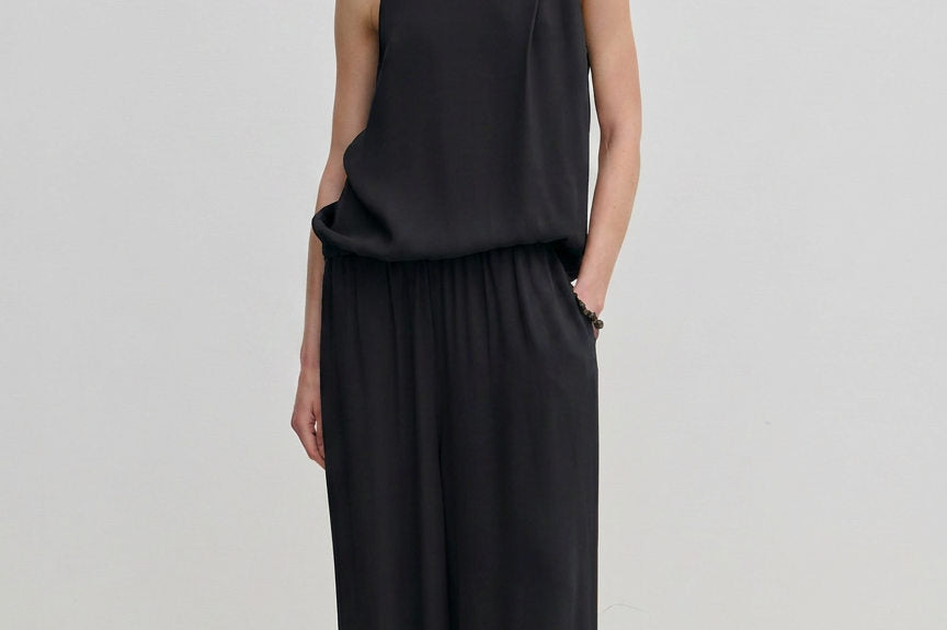 A person wearing a sleeveless black turtleneck top and matching black Nya Pants with an elasticated waist and loose-fitting, balloon leg silhouette.