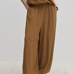 Person wearing brown Nya Pants with a balloon leg, elastic waistband, and tucked-in matching top, paired with off-white shoes.