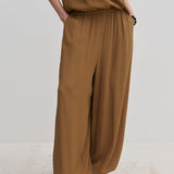 Person wearing brown Nya Pants with a balloon leg, elastic waistband, and tucked-in matching top, paired with off-white shoes.