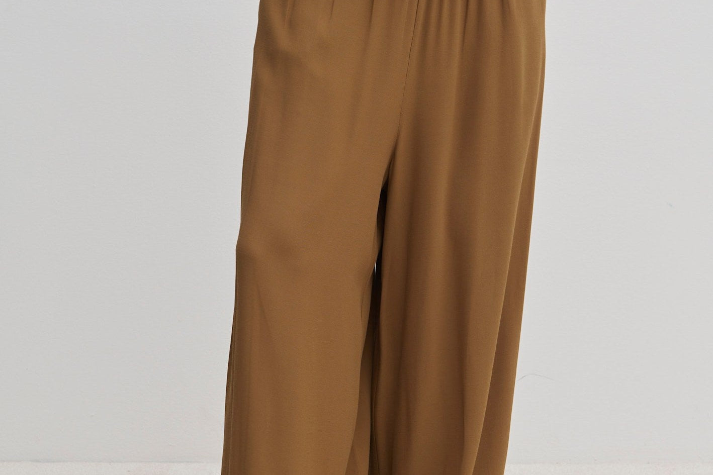 Person wearing brown Nya Pants with a balloon leg, elastic waistband, and tucked-in matching top, paired with off-white shoes.