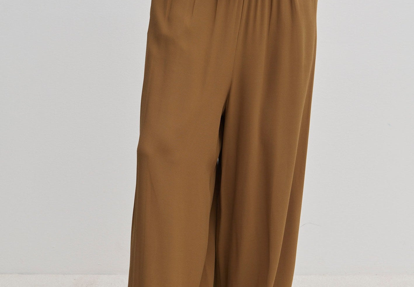 Person wearing brown Nya Pants with a balloon leg, elastic waistband, and tucked-in matching top, paired with off-white shoes.