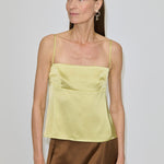 A woman wearing a pale yellow Angela Top with a square neckline and a brown skirt.