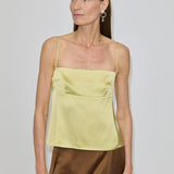 A woman wearing a pale yellow Angela Top with a square neckline and a brown skirt.