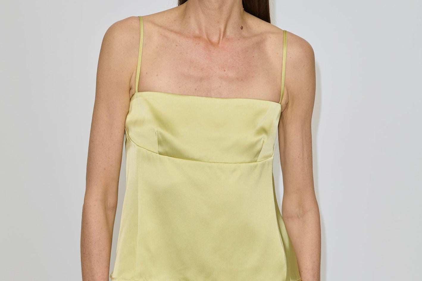 A woman wearing a pale yellow Angela Top with a square neckline and a brown skirt.