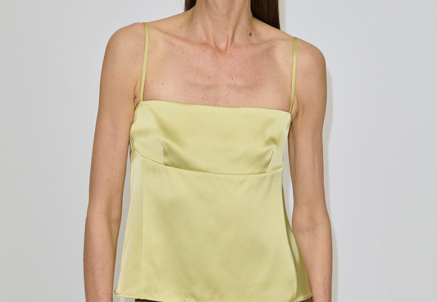 A woman wearing a pale yellow Angela Top with a square neckline and a brown skirt.