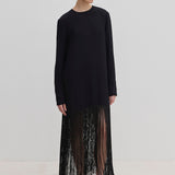 The Aris Dress by Herskind ApS is a long-sleeved black shift dress with a crew neckline and an ankle-length fringe hem, styled with black mules.