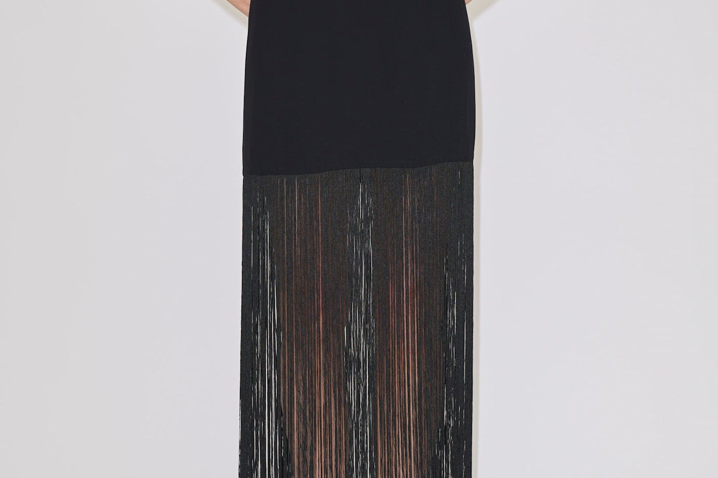The Herskind ApS Olivia Skirt is a black high-waisted midi skirt with long, sheer fringe at the hem, worn with a matching sleeveless top and cream heels.
