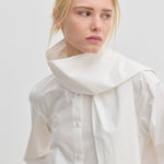 The Natalia Shirt by Herskind ApS is an oversized white cotton button-up with an attached scarf-like collar piece draped around the neck.