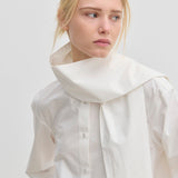 The Natalia Shirt by Herskind ApS is an oversized white cotton button-up with an attached scarf-like collar piece draped around the neck.