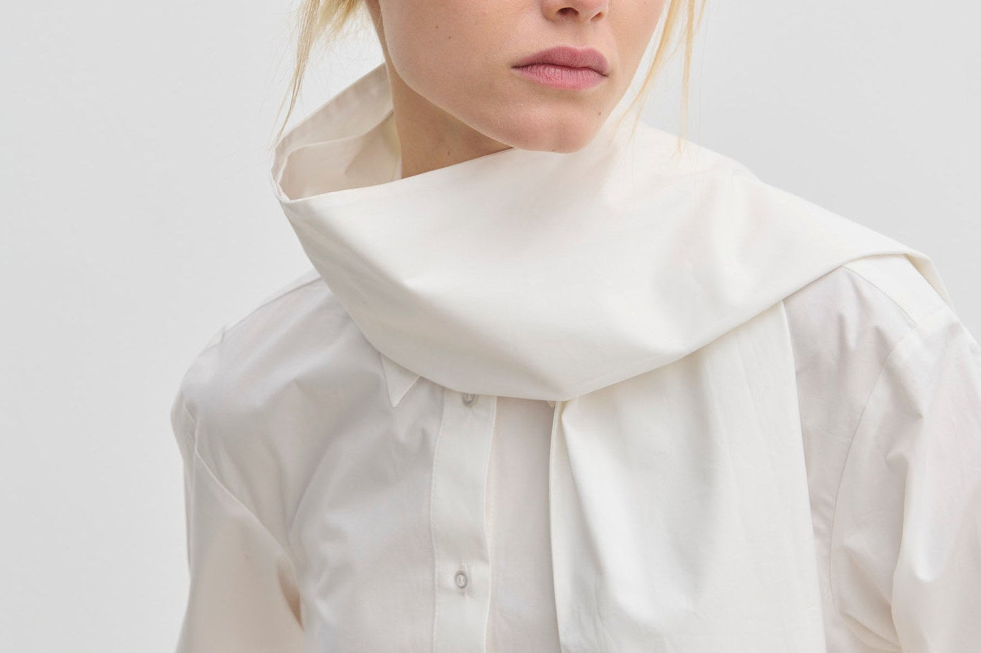 The Natalia Shirt by Herskind ApS is an oversized white cotton button-up with an attached scarf-like collar piece draped around the neck.