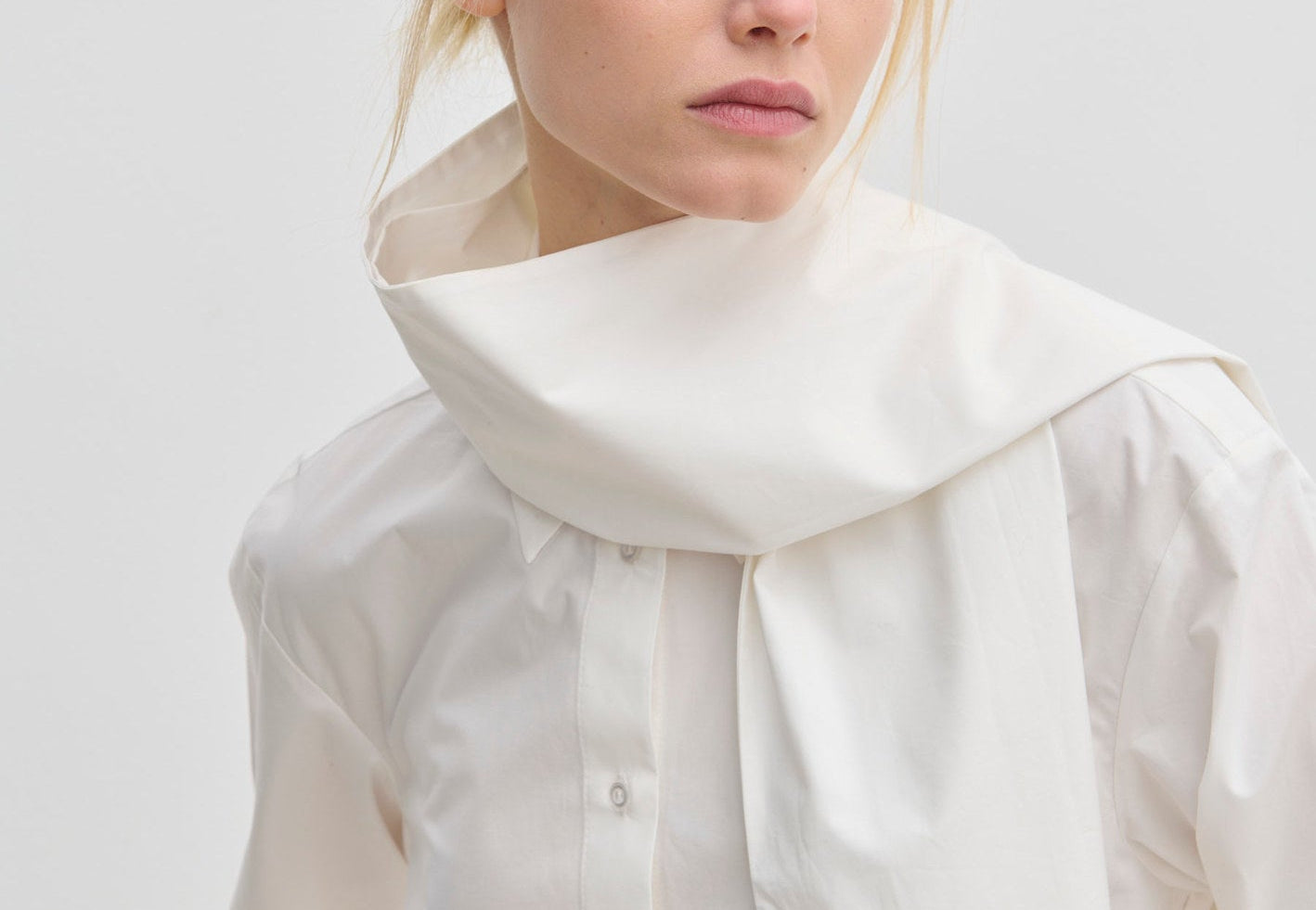 The Natalia Shirt by Herskind ApS is an oversized white cotton button-up with an attached scarf-like collar piece draped around the neck.